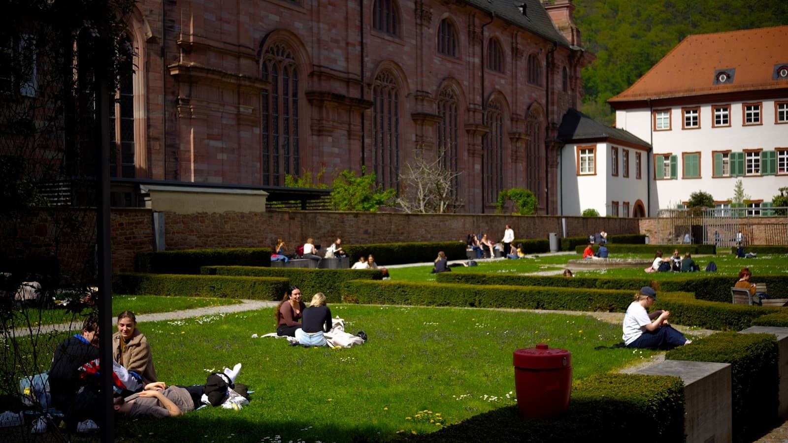 Students relaxing and studying on a landscaped campus lawn in front of a large stone building, no readable signage.