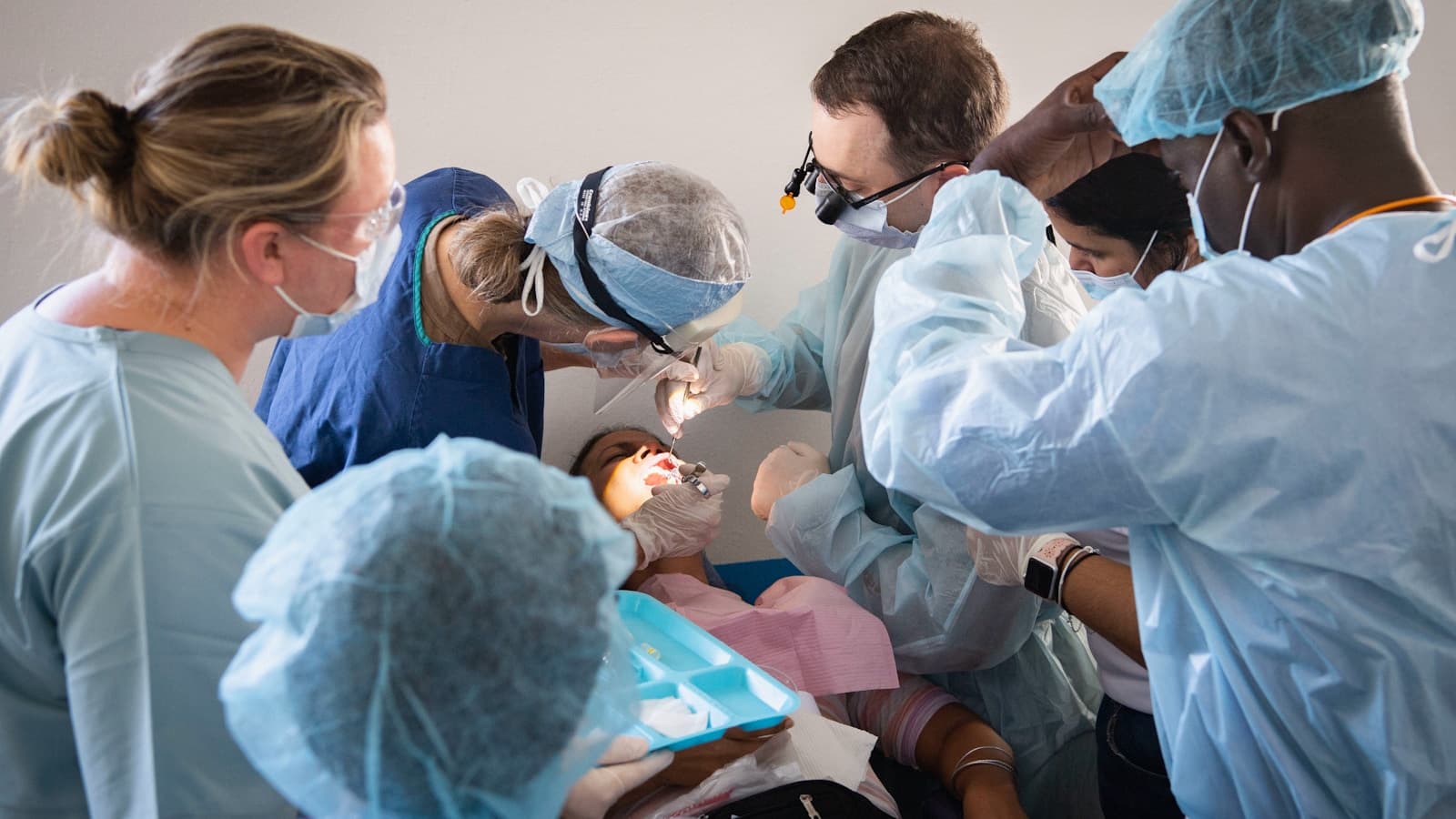A team of dental professionals in scrubs and masks performing a procedure on a patient.