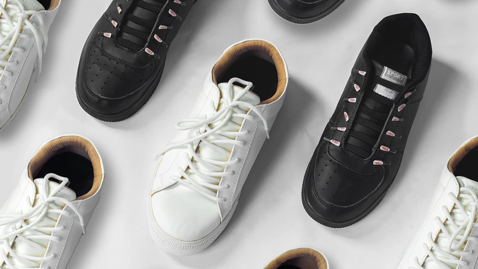 Overhead array of plain black and white leather sneakers on a white surface.