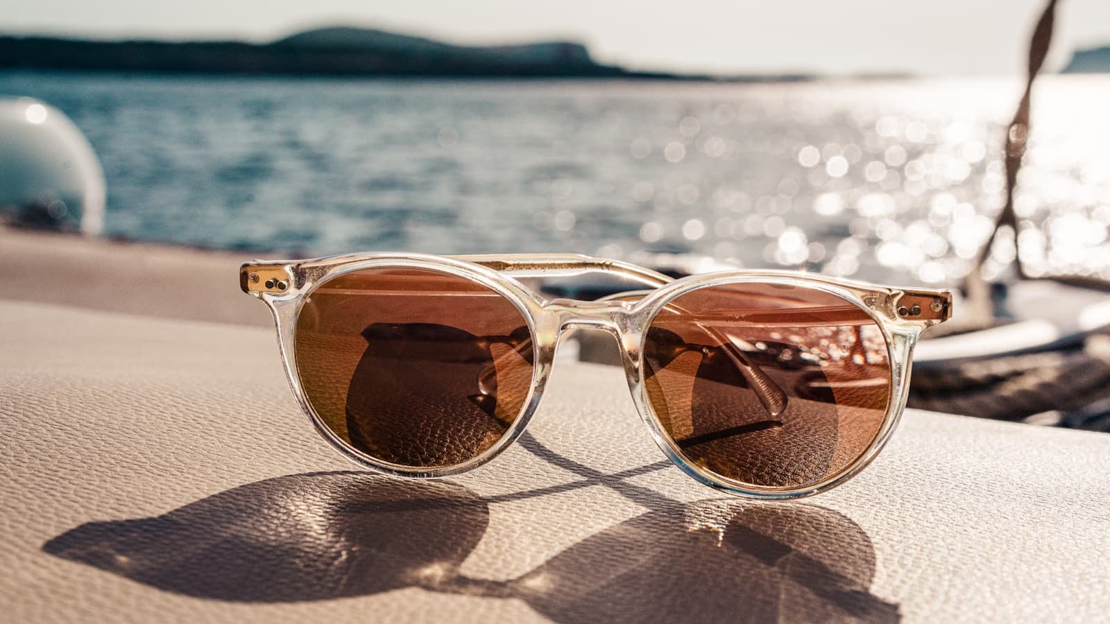 Clear-frame sunglasses in warm sunlight with a waterfront backdrop.