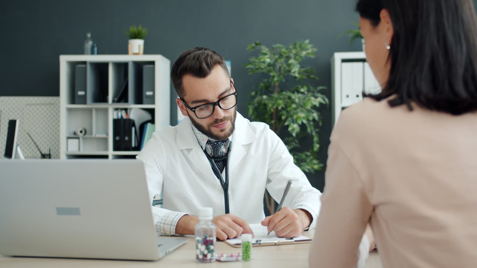 A modern doctor's office, physician with a laptop talking calmly with a patient.