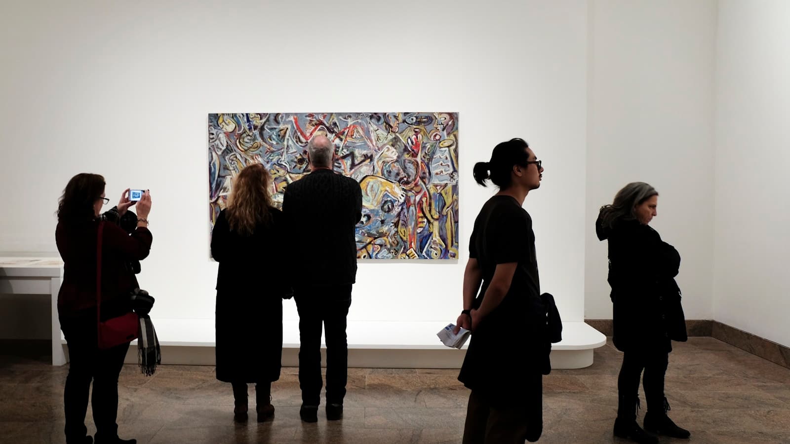 Visitors standing before a large abstract painting on a white gallery wall.