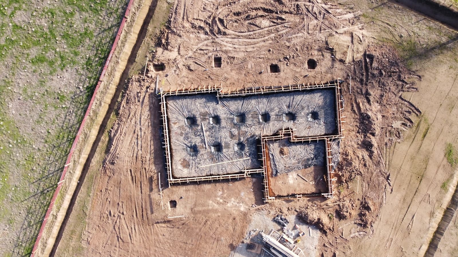 An aerial view of a freshly poured concrete house foundation surrounded by dirt and framing, with no people, text, or logos visible.