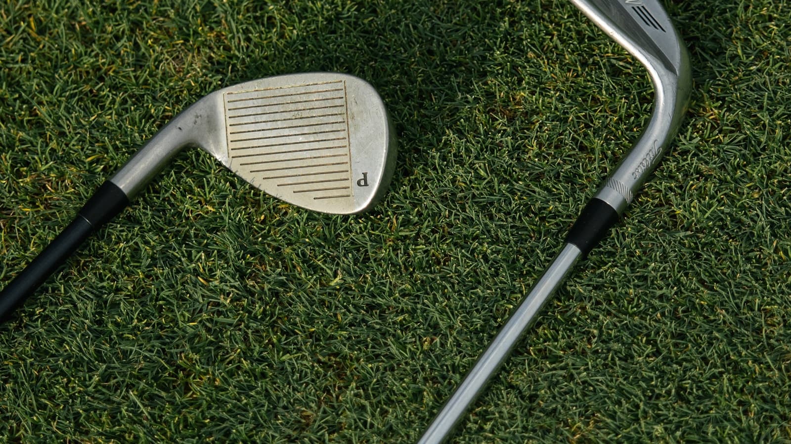 A single golf iron head resting on green grass beside another club.