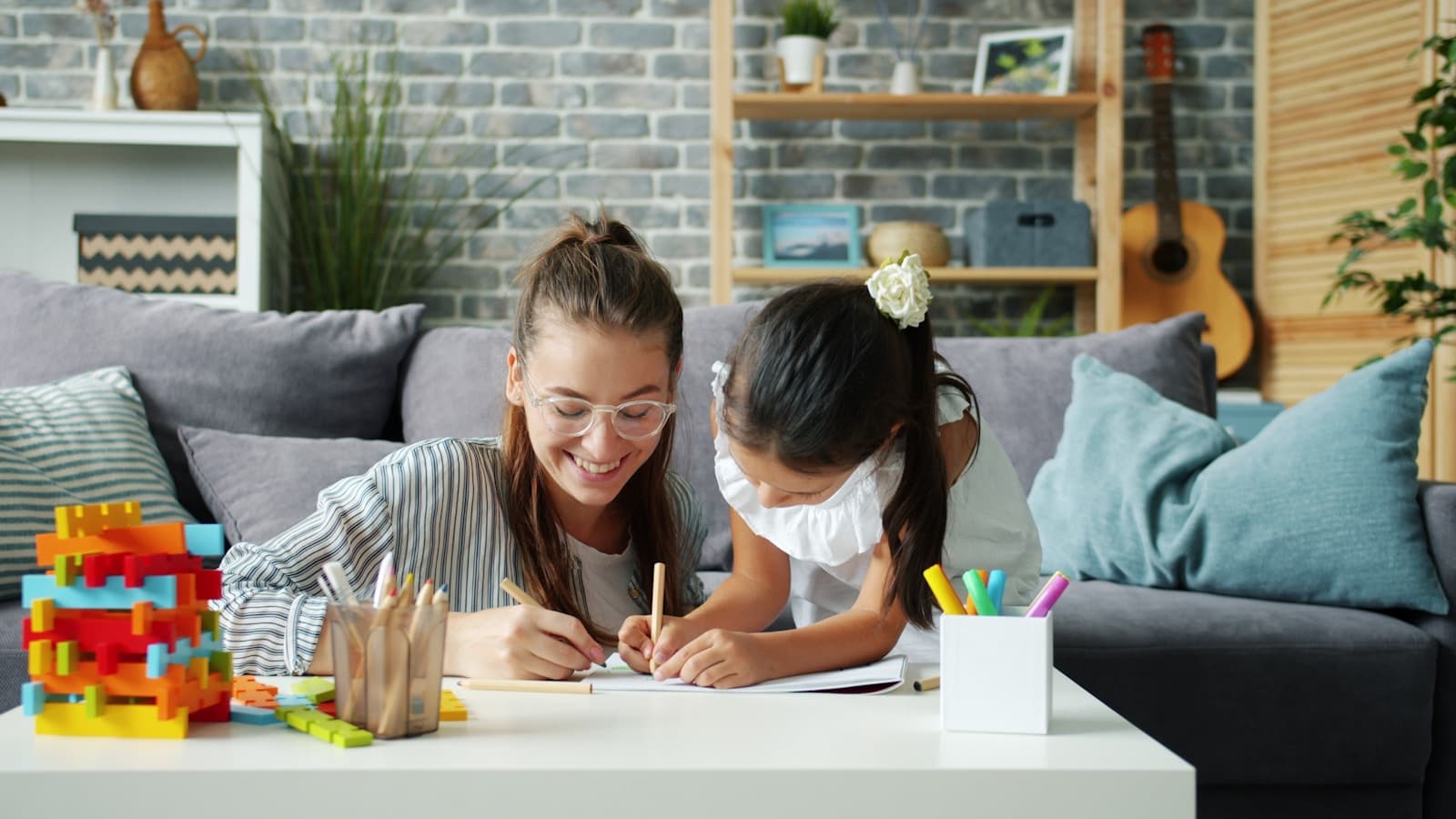 A mother and daughter drawing together on a couch in a cozy modern living room.