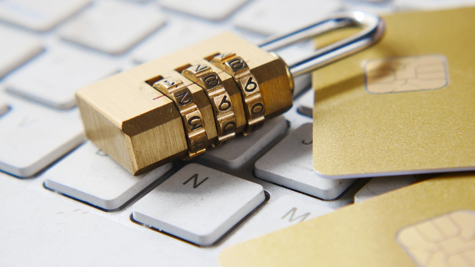 A gold combination padlock resting on a laptop keyboard next to credit cards.
