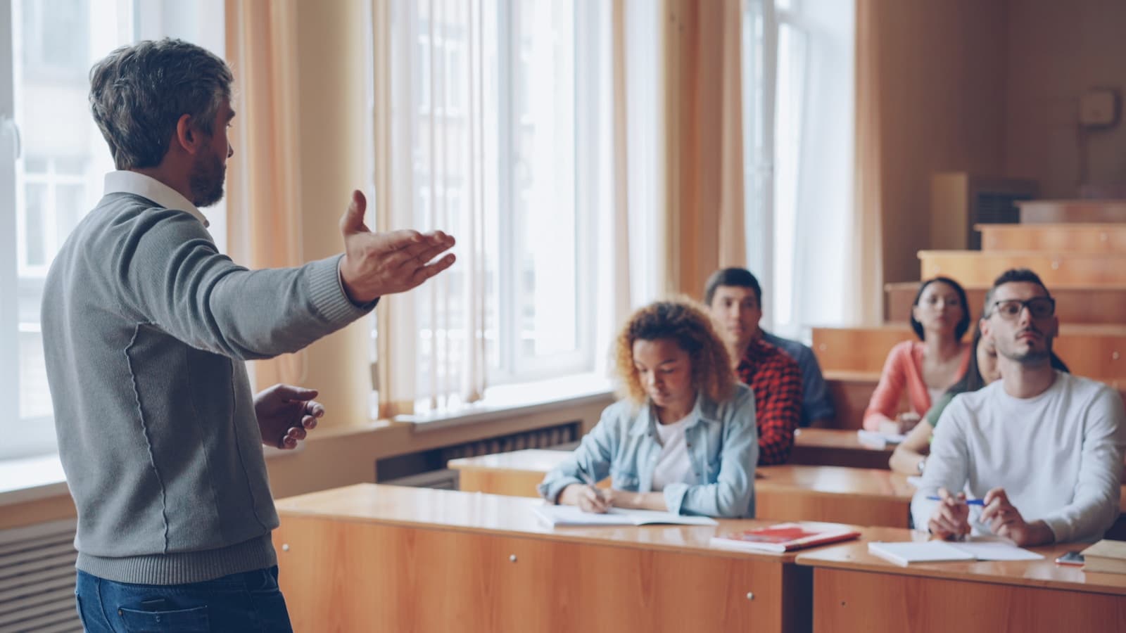 A bearded professor gesturing while lecturing to seated students.