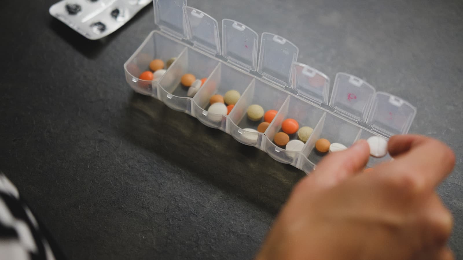 A person picking medication out of a weekly pill organizer.