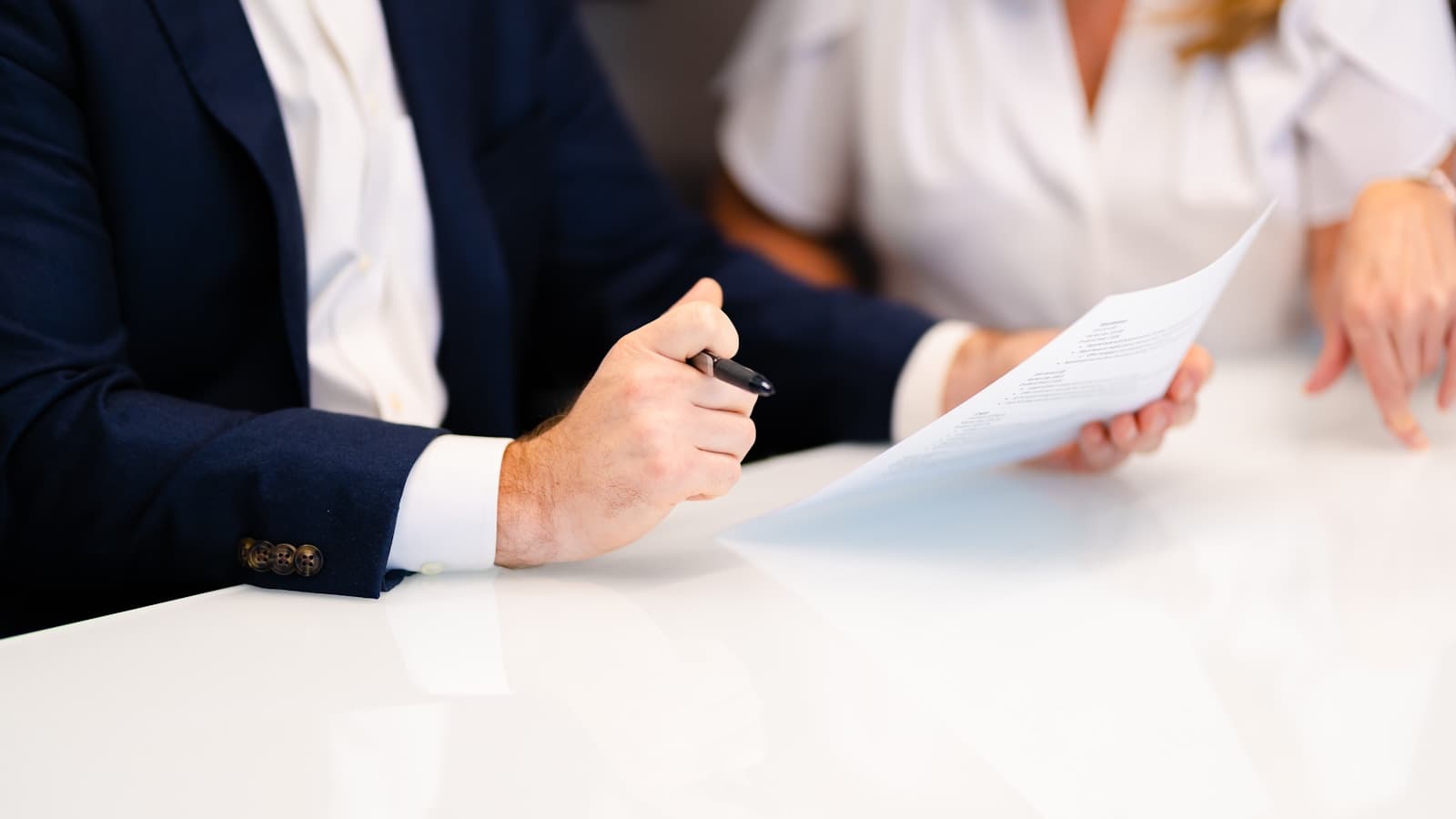 A man and woman in a serious professional consultation at a white table.