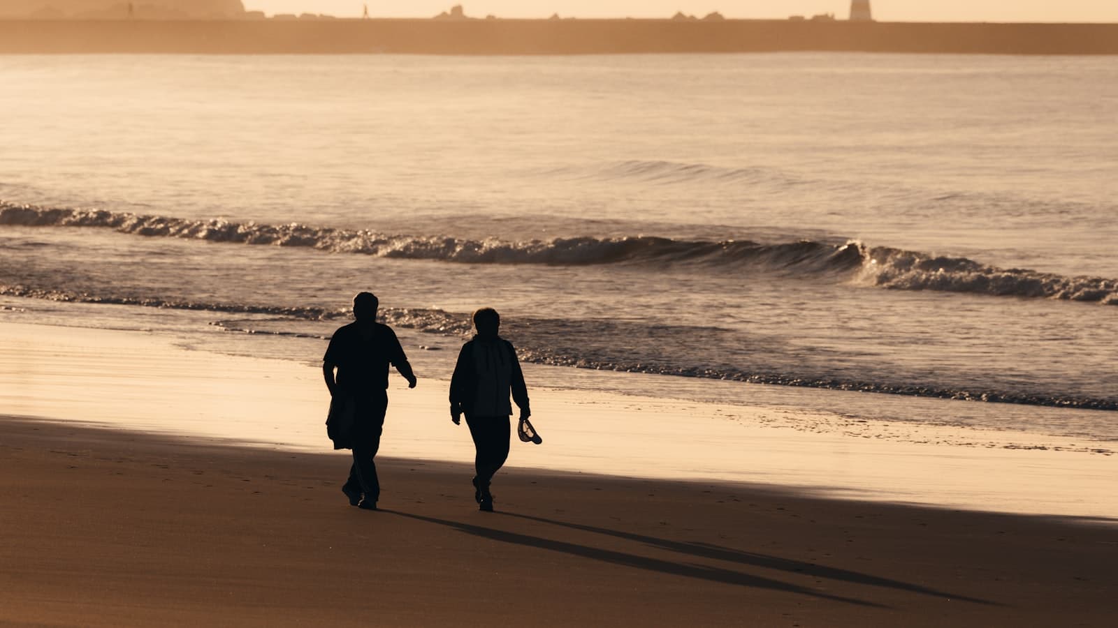 A fully silhouetted couple walking away along a beach at sunset, faces not visible, no text or logos.