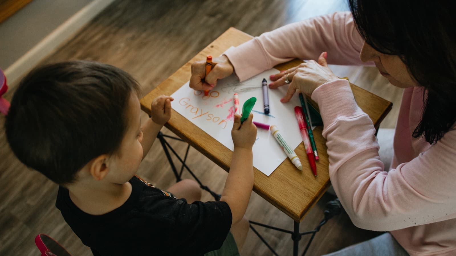 An adult and child coloring together at a table, overhead angle.