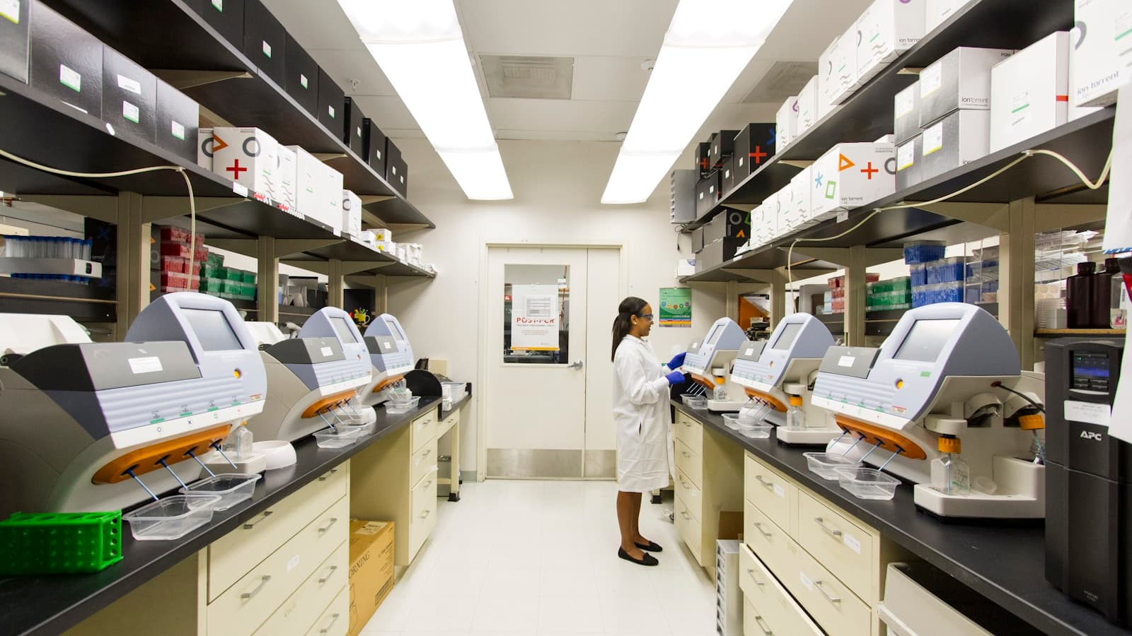 A technician in a lab coat working with modern genomic lab equipment.