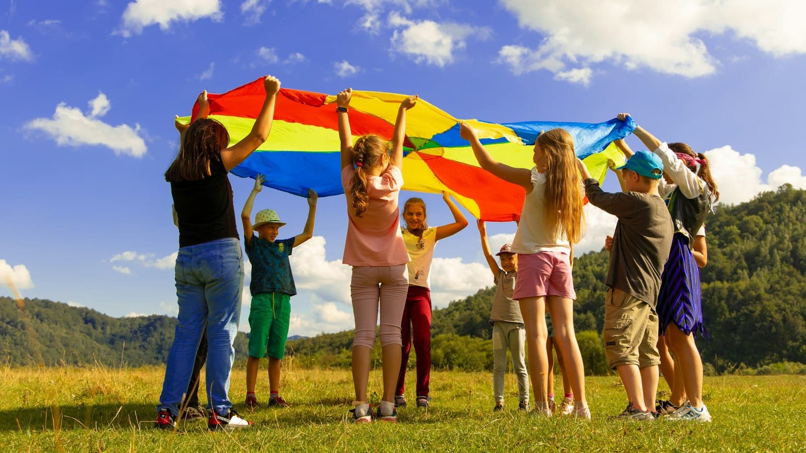 A group of children playing with a large colorful parachute outdoors on grass.
