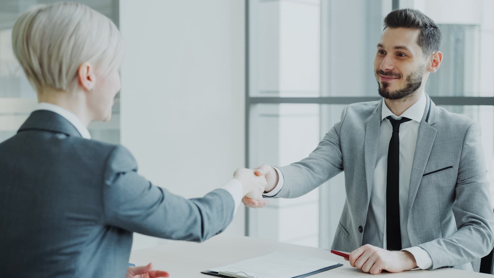Two professionals shaking hands across a table after a discussion.