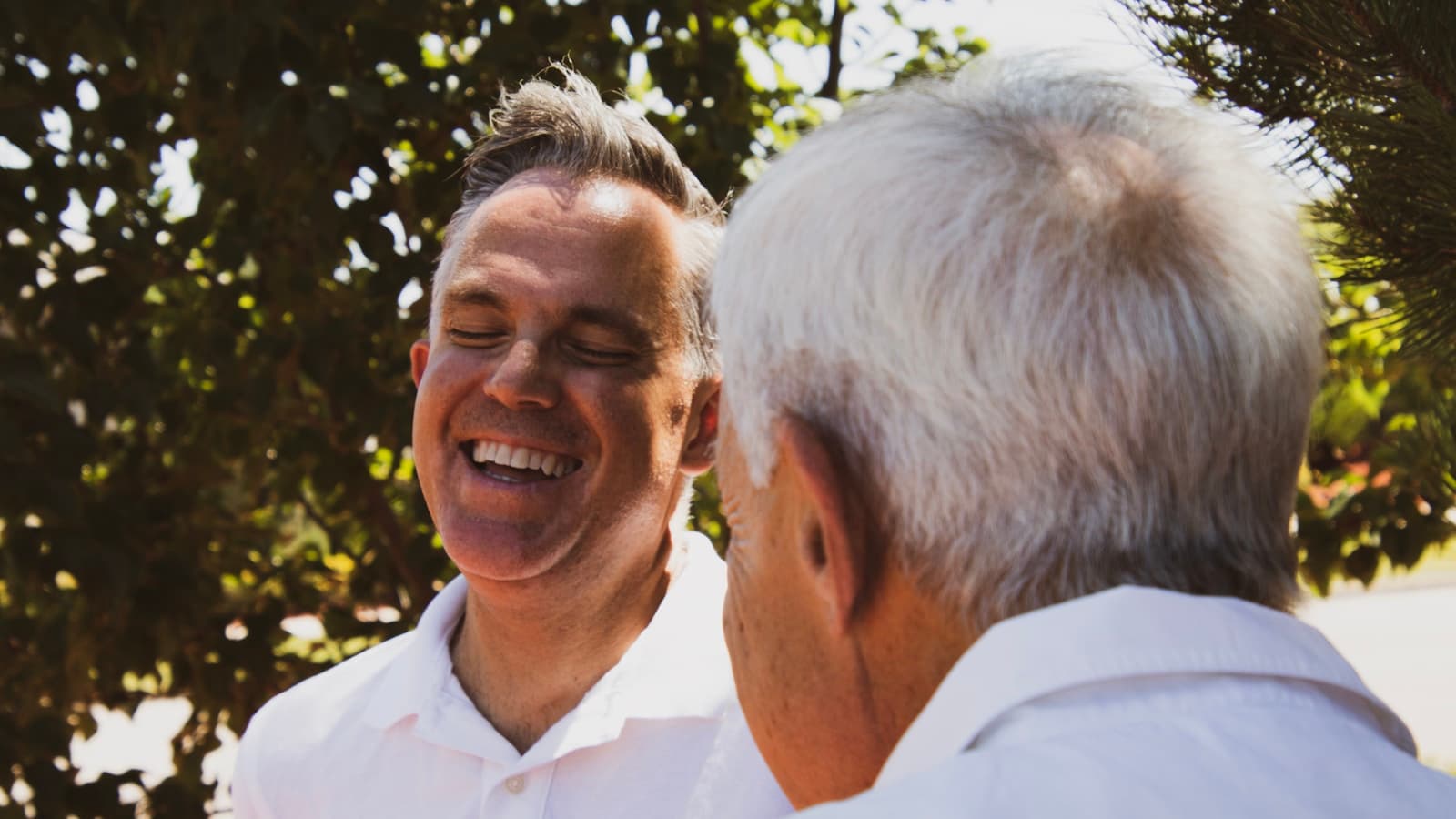 A middle-aged son laughing warmly with his older father outdoors.