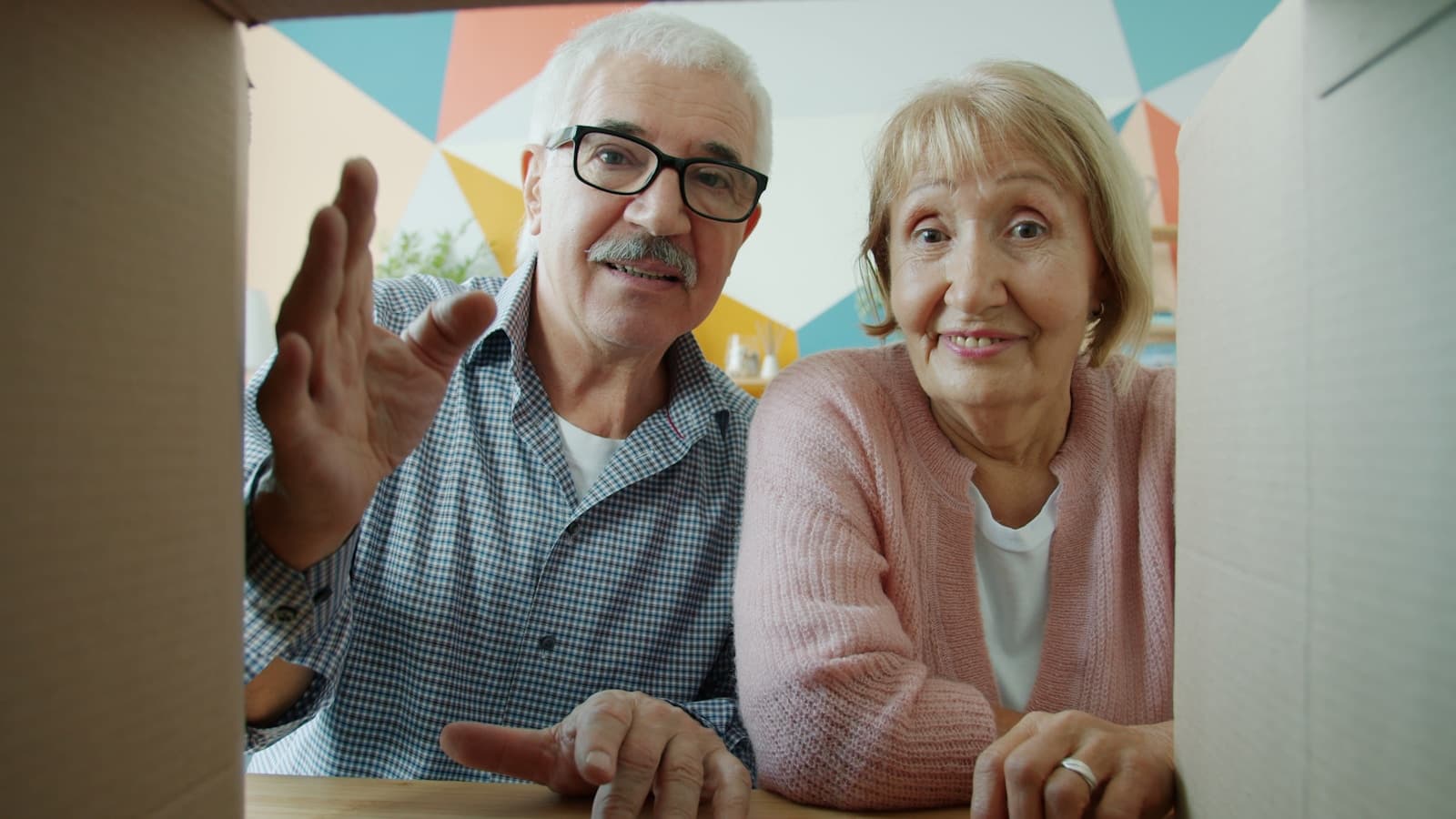 An older couple looking into a cardboard box together, warm and cheerful.