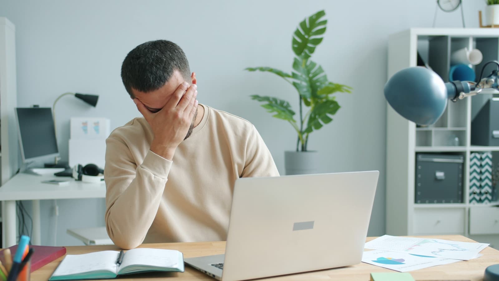 A man at a home desk with a laptop, head in hand, stressed.