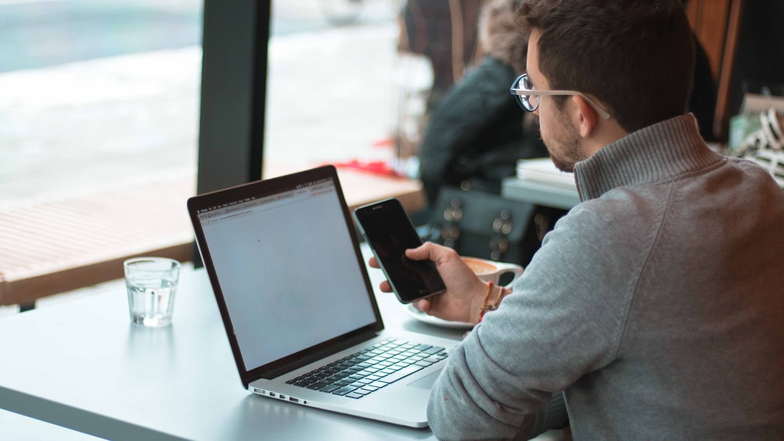 A person working on a laptop at a cafe table by a window.