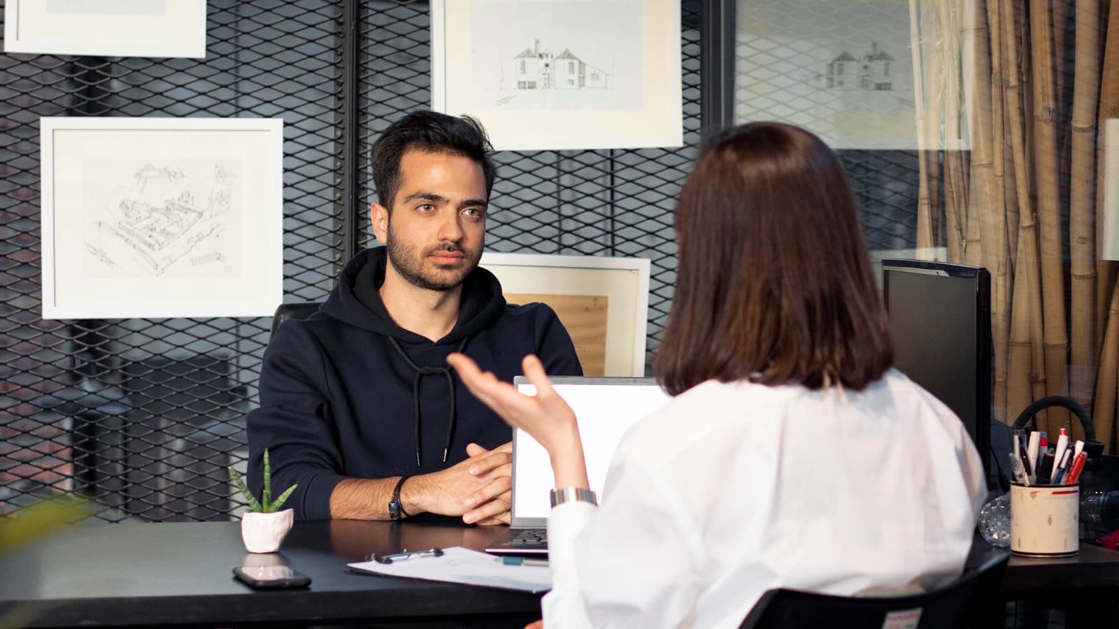 A man and woman having a serious conversation across a desk with a laptop.