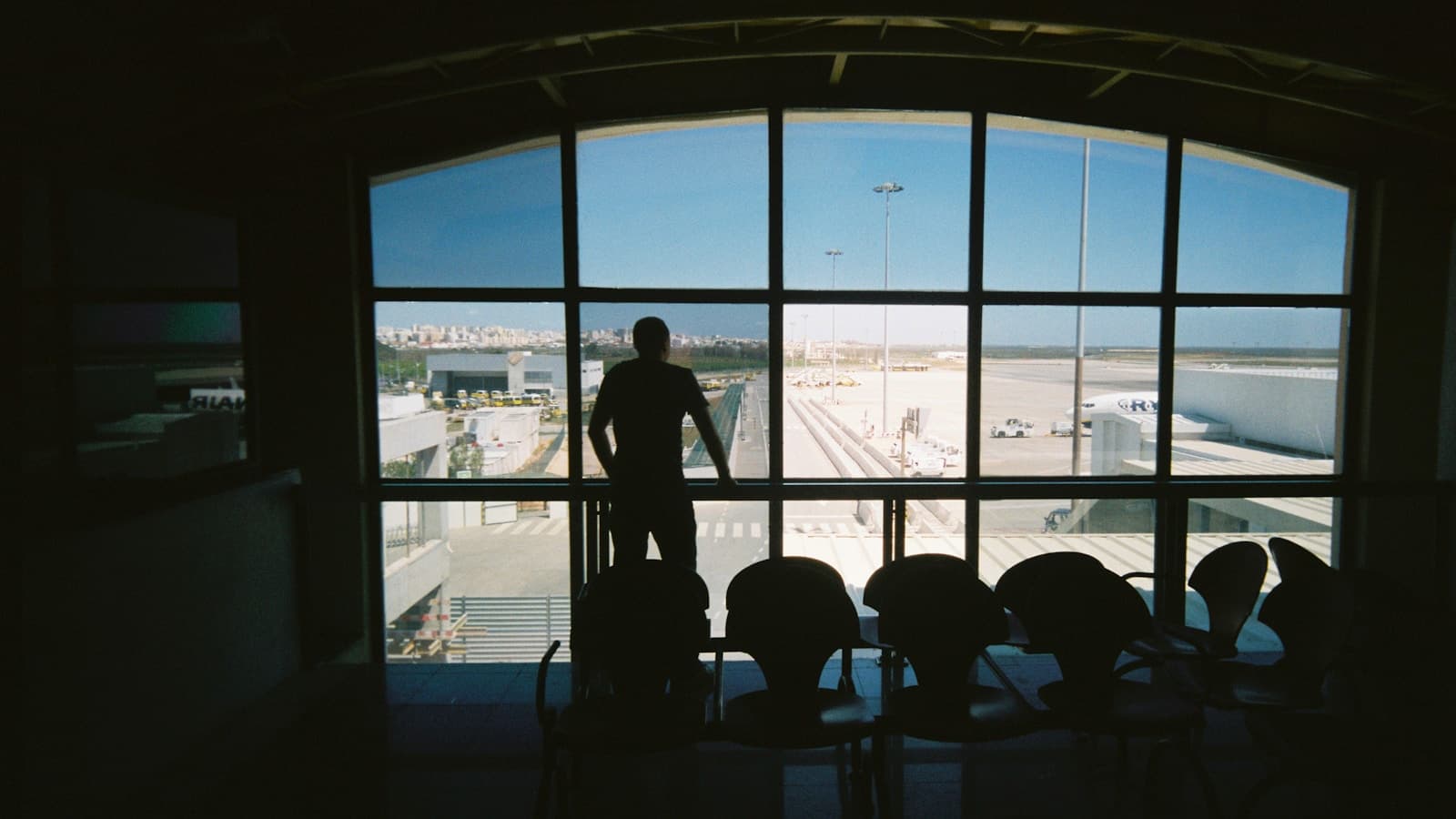 A silhouette of a man standing at an airport terminal window watching the runway.