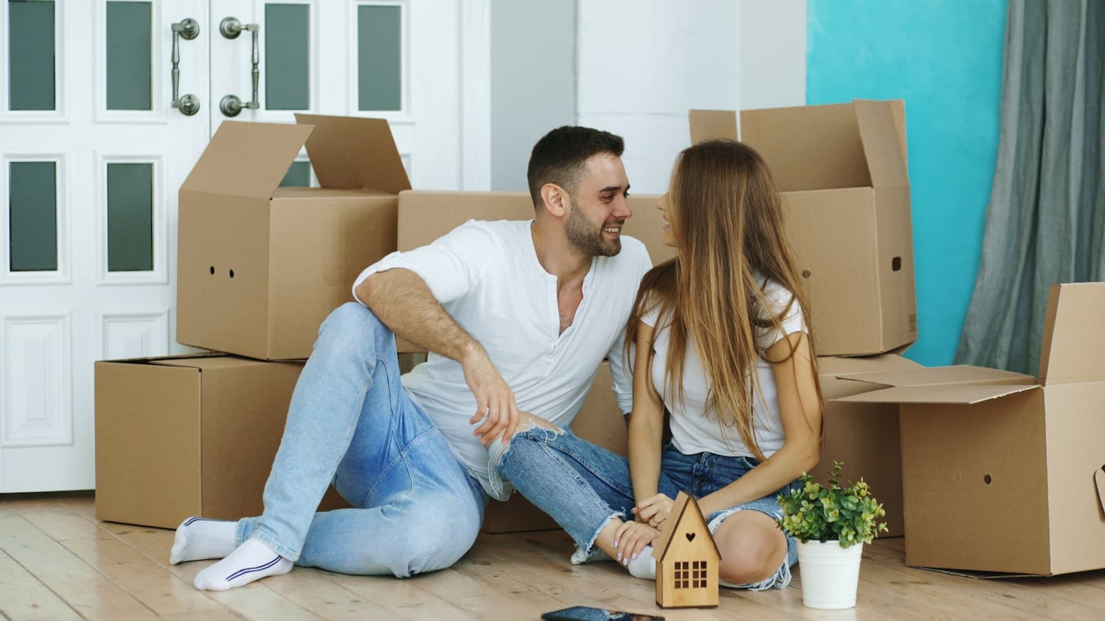 A happy couple sitting on the floor amid moving boxes, laughing together.