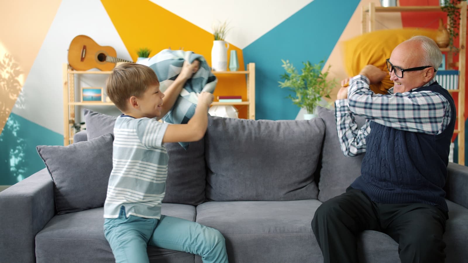 A grandfather and grandson having a joyful pillow fight on the couch.