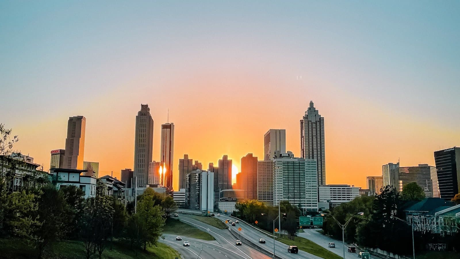 The Atlanta skyline at sunset viewed from the Jackson Street Bridge, with downtown high-rises and a highway in the foreground.