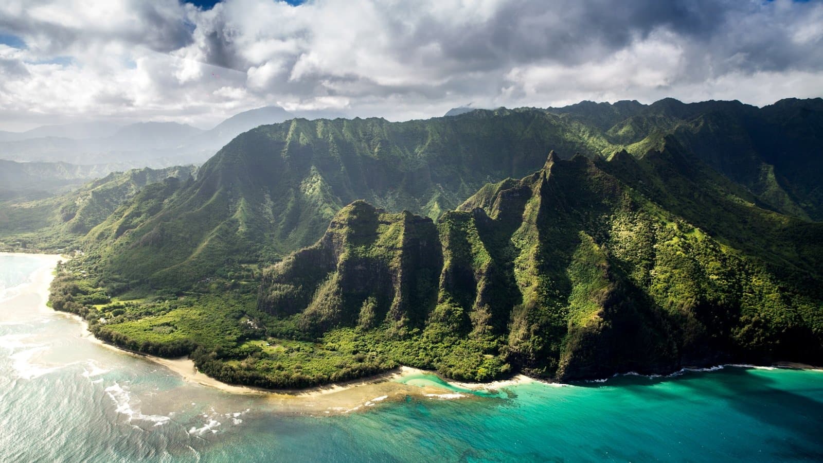 An aerial shot of the lush green Na Pali Coast cliffs meeting turquoise water in Kauai.