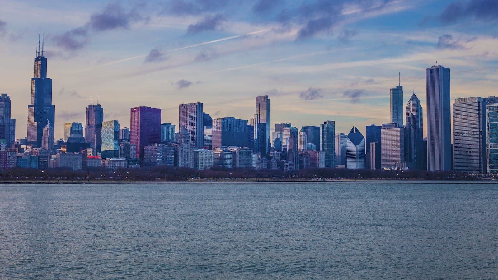 The Chicago skyline, including Willis Tower, viewed across Lake Michigan at dusk.