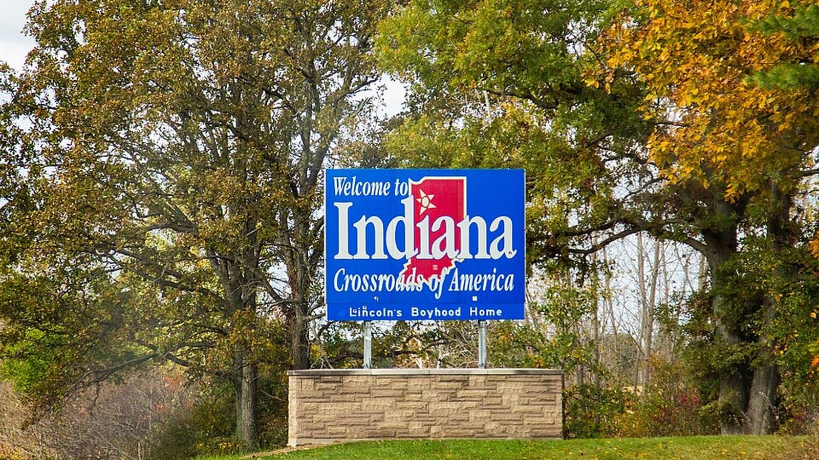 A blue "Welcome to Indiana - Crossroads of America" highway sign along I-80 near Angola, framed by autumn trees.