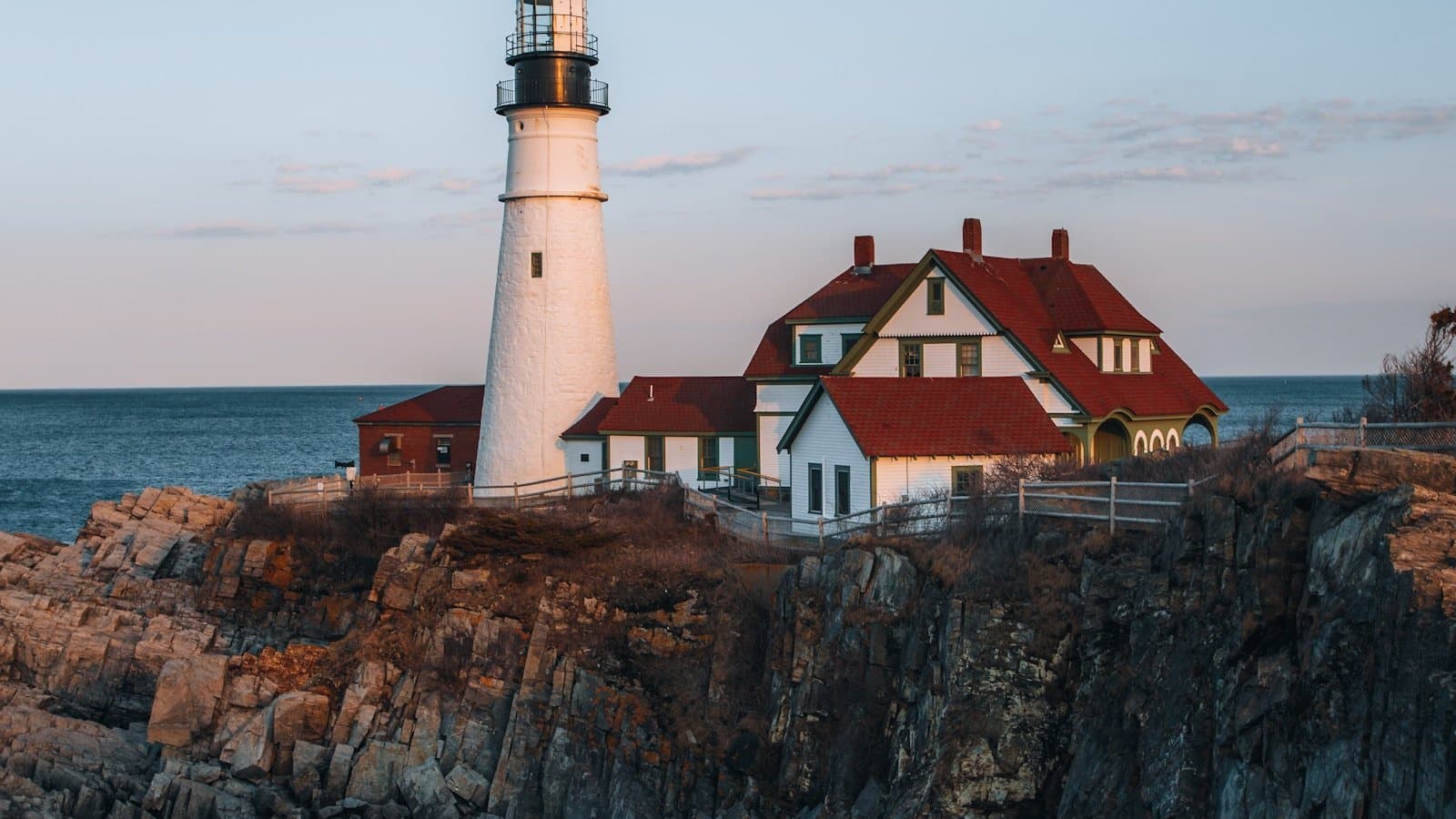 Portland Head Light, Maine's iconic white lighthouse and keeper's house perched on a rocky Atlantic cliff at dusk.