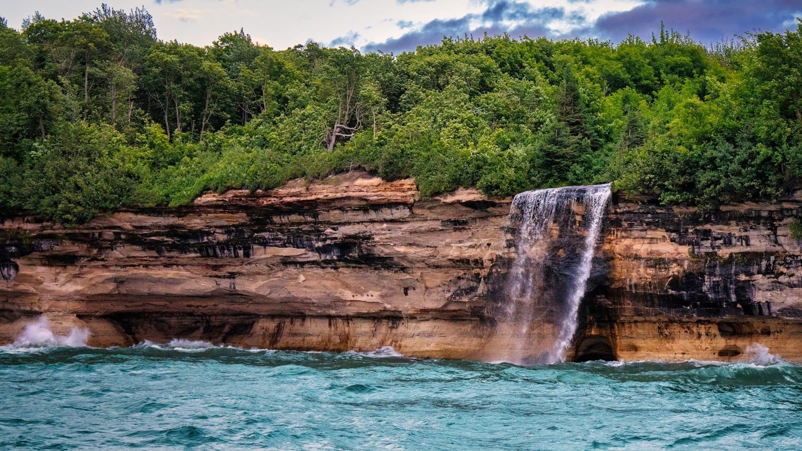 A waterfall spilling over multicolored sandstone cliffs at Pictured Rocks National Lakeshore on Lake Superior.