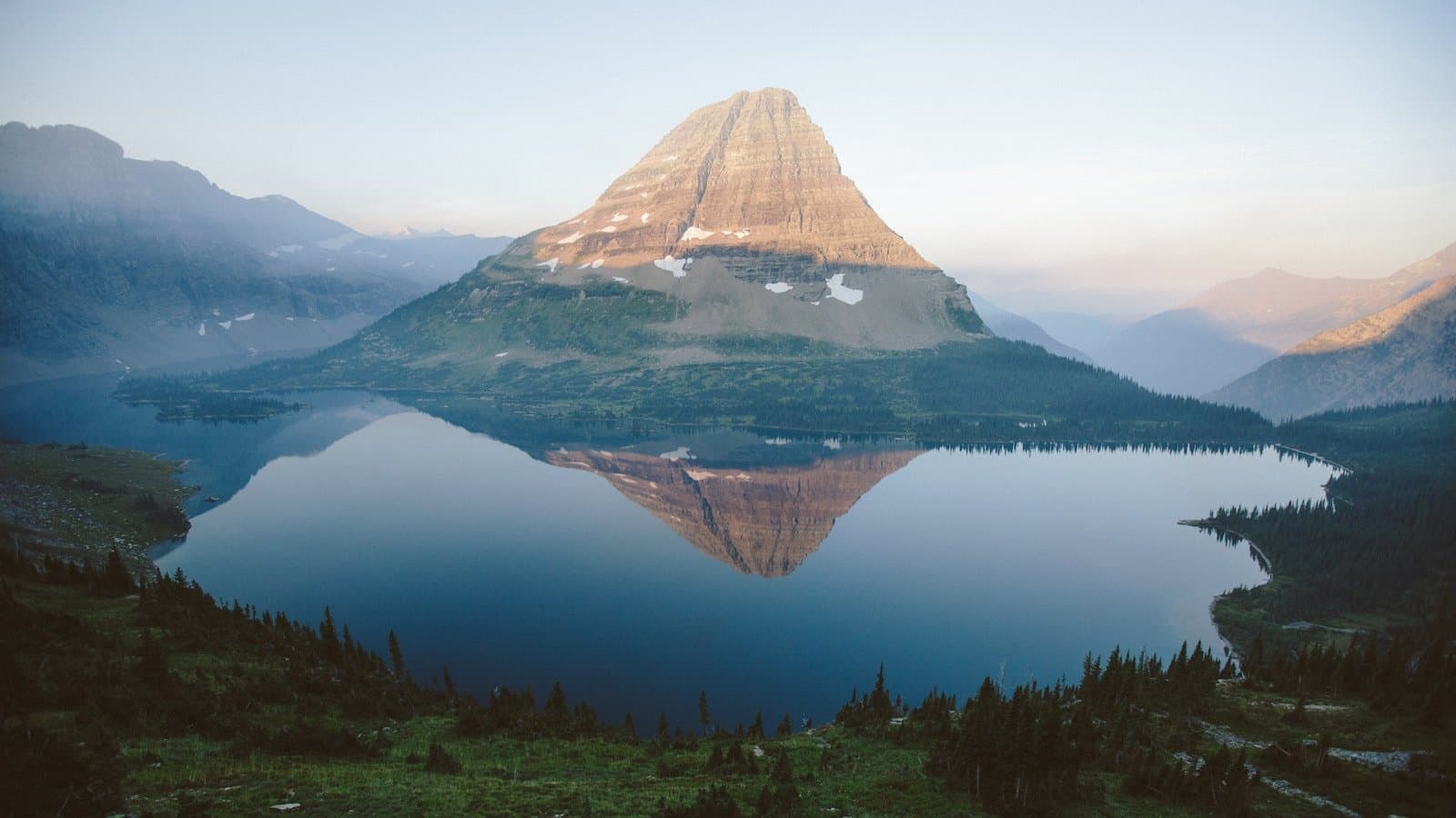Hidden Lake and its namesake pyramidal peak reflected in still water at sunrise, Glacier National Park, Montana.