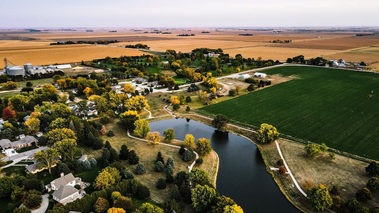 An autumn aerial view of farmland, a pond, and a small town near Henderson, Nebraska, with golden harvest fields stretching to the horizon.
