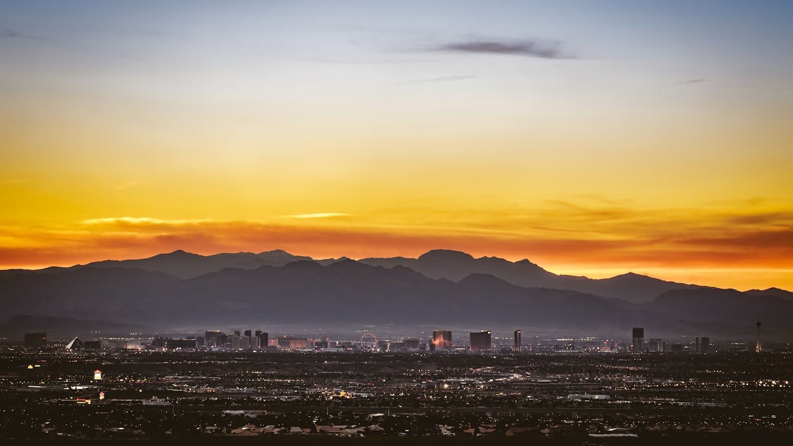 The Las Vegas skyline and Strip silhouetted at sunset against the surrounding desert mountains, shot from a distance.