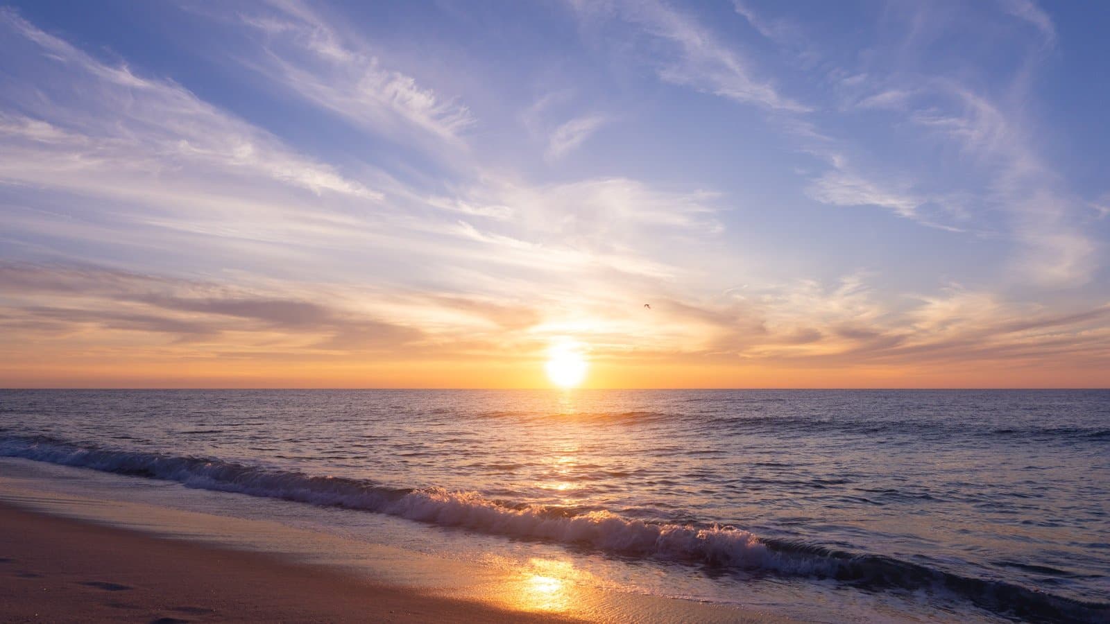 A quiet Jersey Shore beach at sunrise with gentle waves and footprints in the sand.