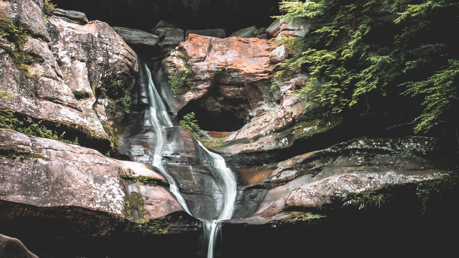 A waterfall cascading through a mossy sandstone grotto at Hocking Hills State Park.