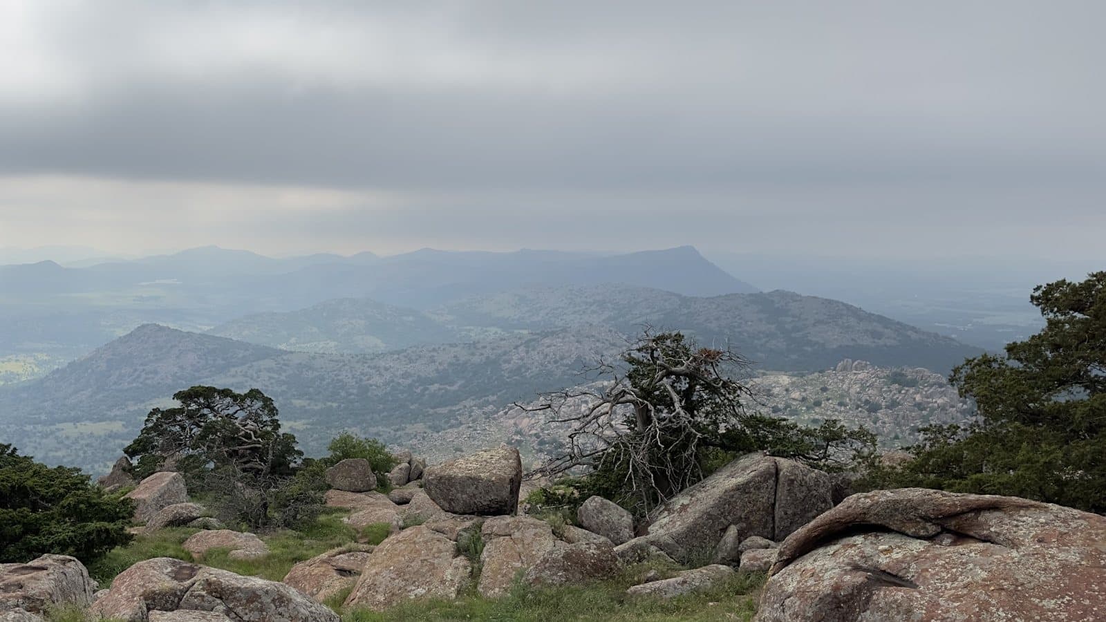 A wide view from atop Mount Scott in the granite Wichita Mountains near Lawton, with boulders and scrubland stretching to a hazy horizon.