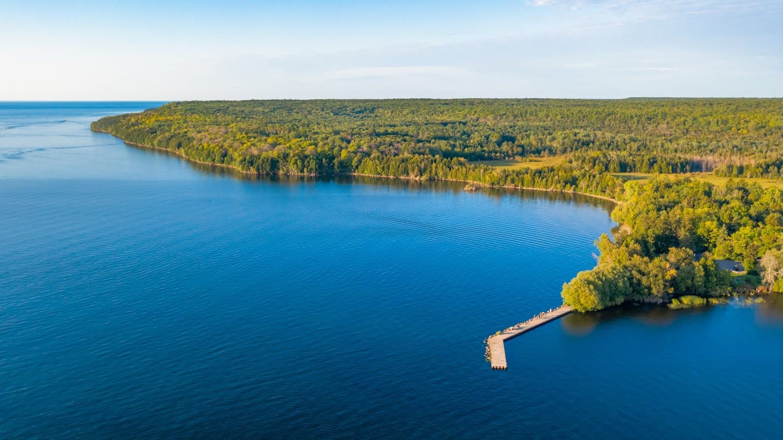 An aerial shot of a forested Door County peninsula meeting the blue waters of Lake Michigan, with a small pier jutting into the water.
