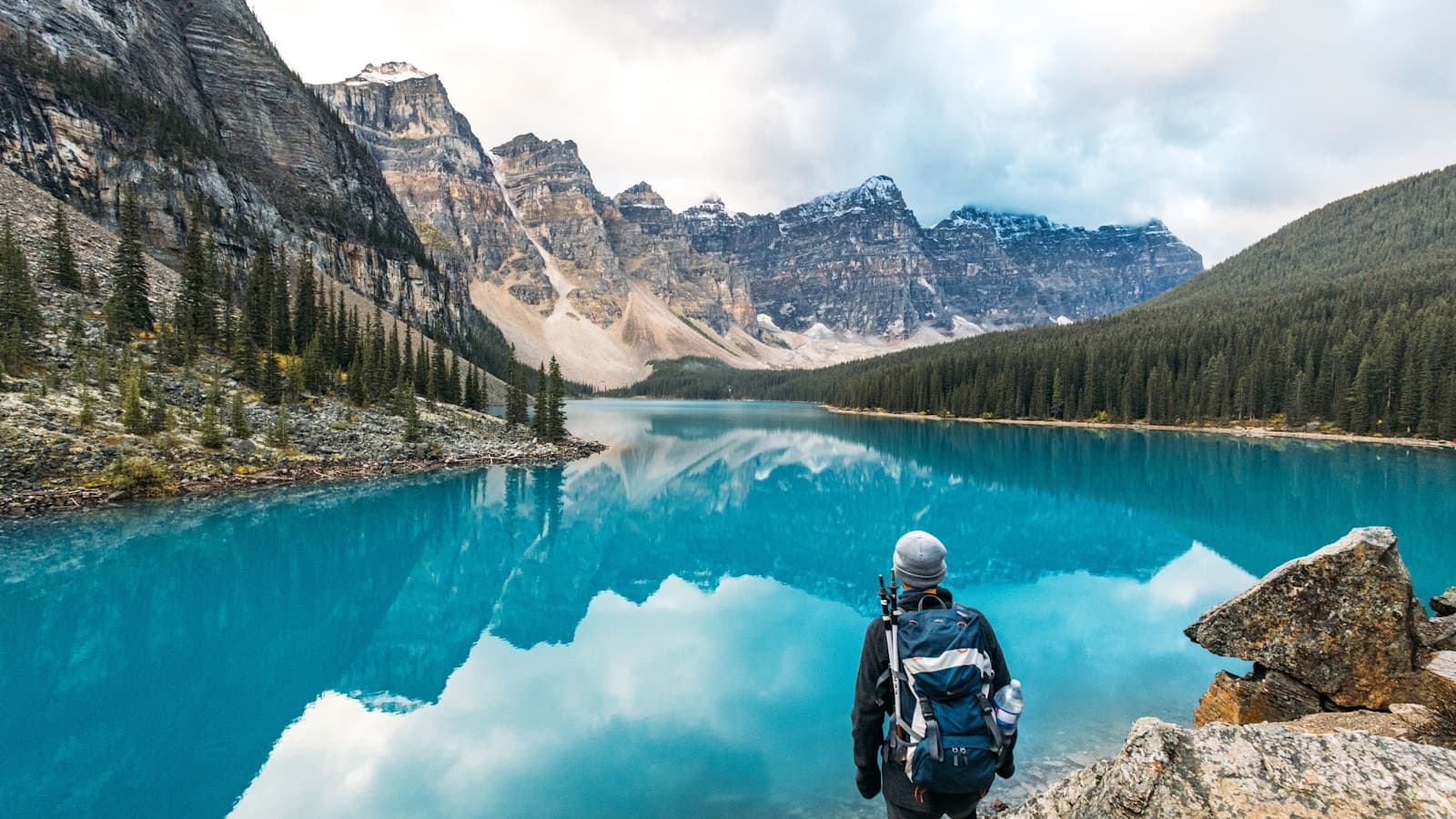 A solo hiker admiring a turquoise mountain lake with a backpack on.