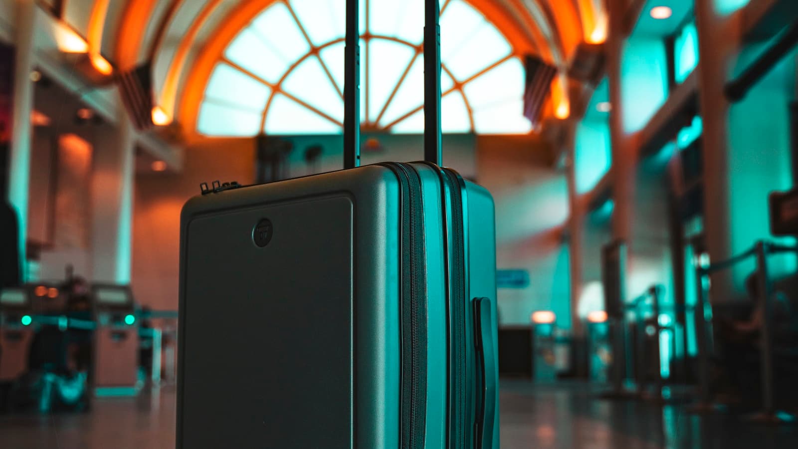 A rolling carry-on suitcase standing alone in an airport terminal hall.