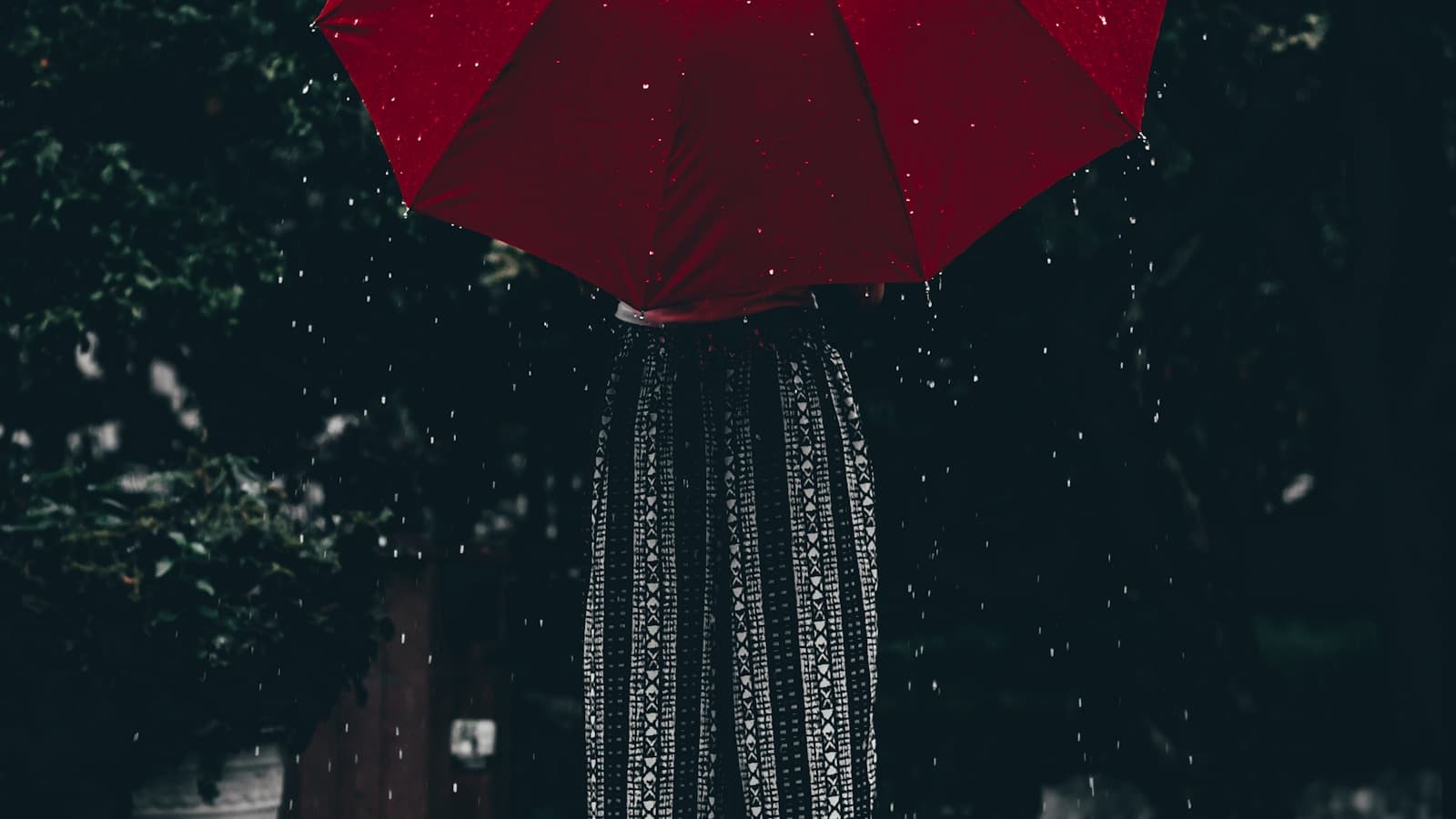 A woman holding a red umbrella standing near a tree, calm and simple.