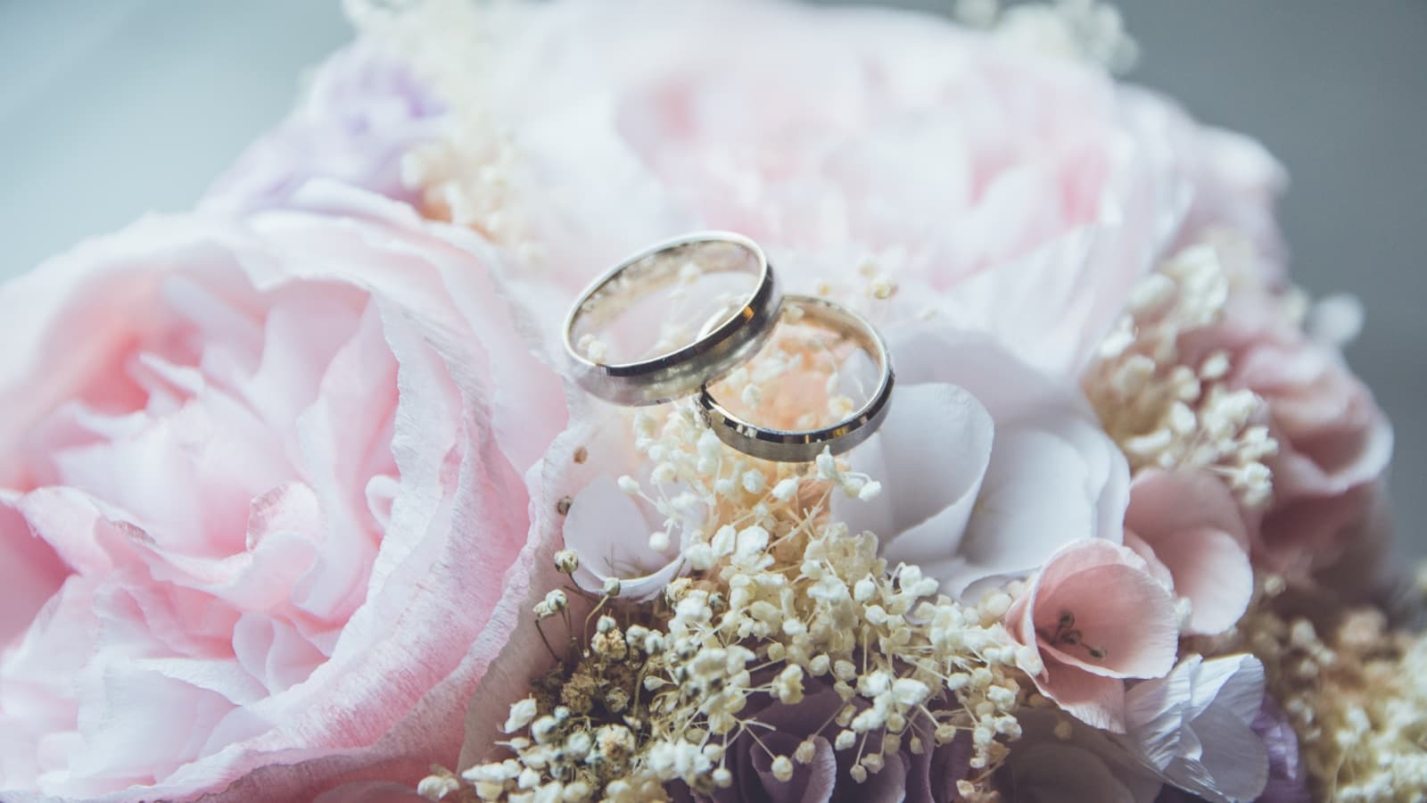 A gold bridal ring set displayed on a pink rose bouquet.