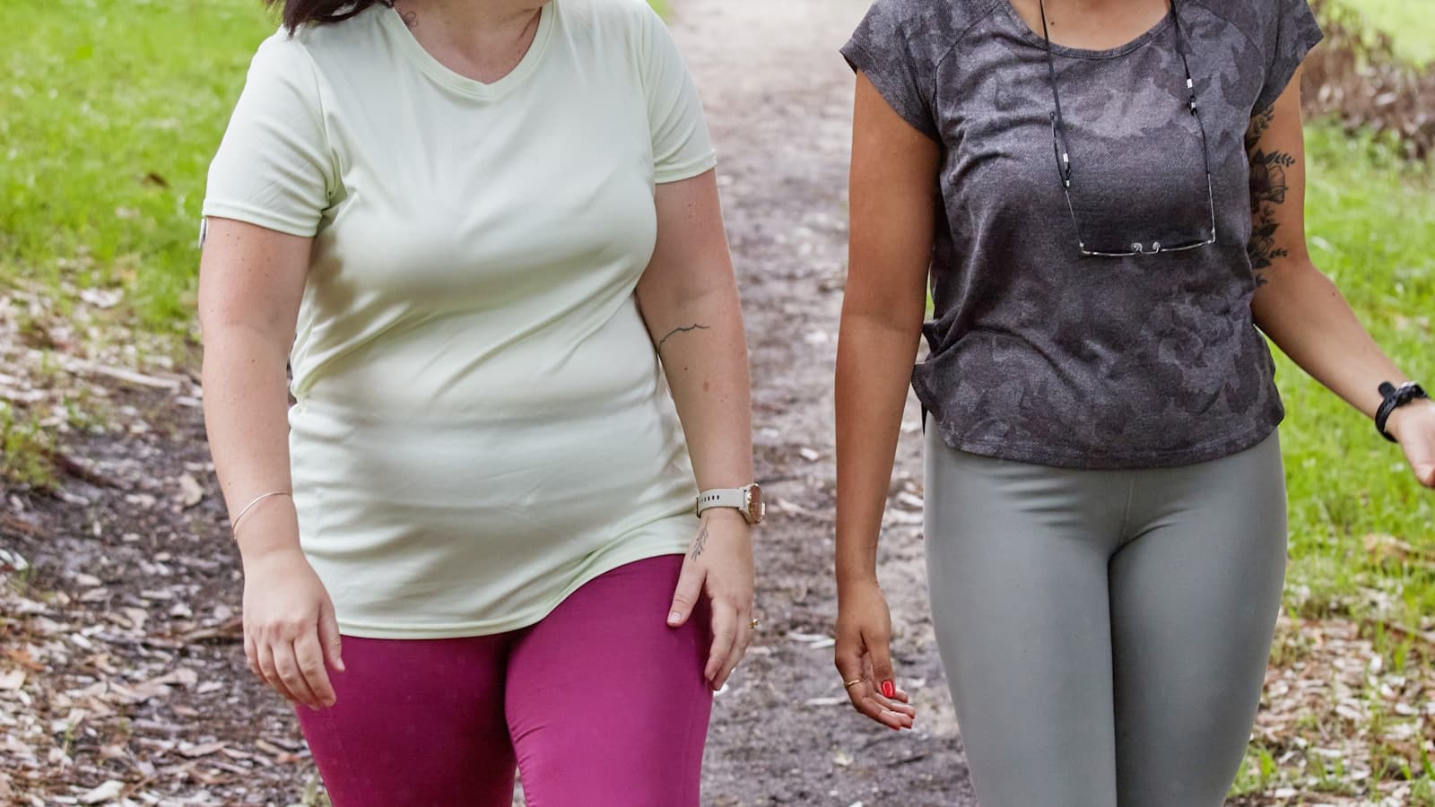 Two smiling women of different body types walking together outdoors, encouraging tone.