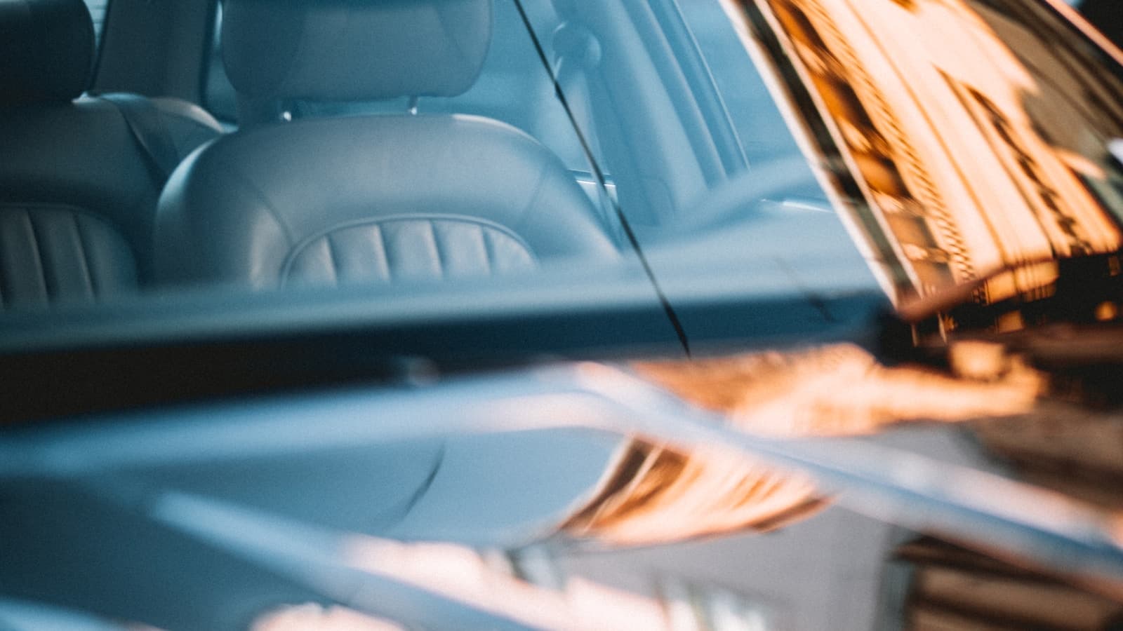 Close-up of a car's tinted side window and glass reflecting warm evening light.