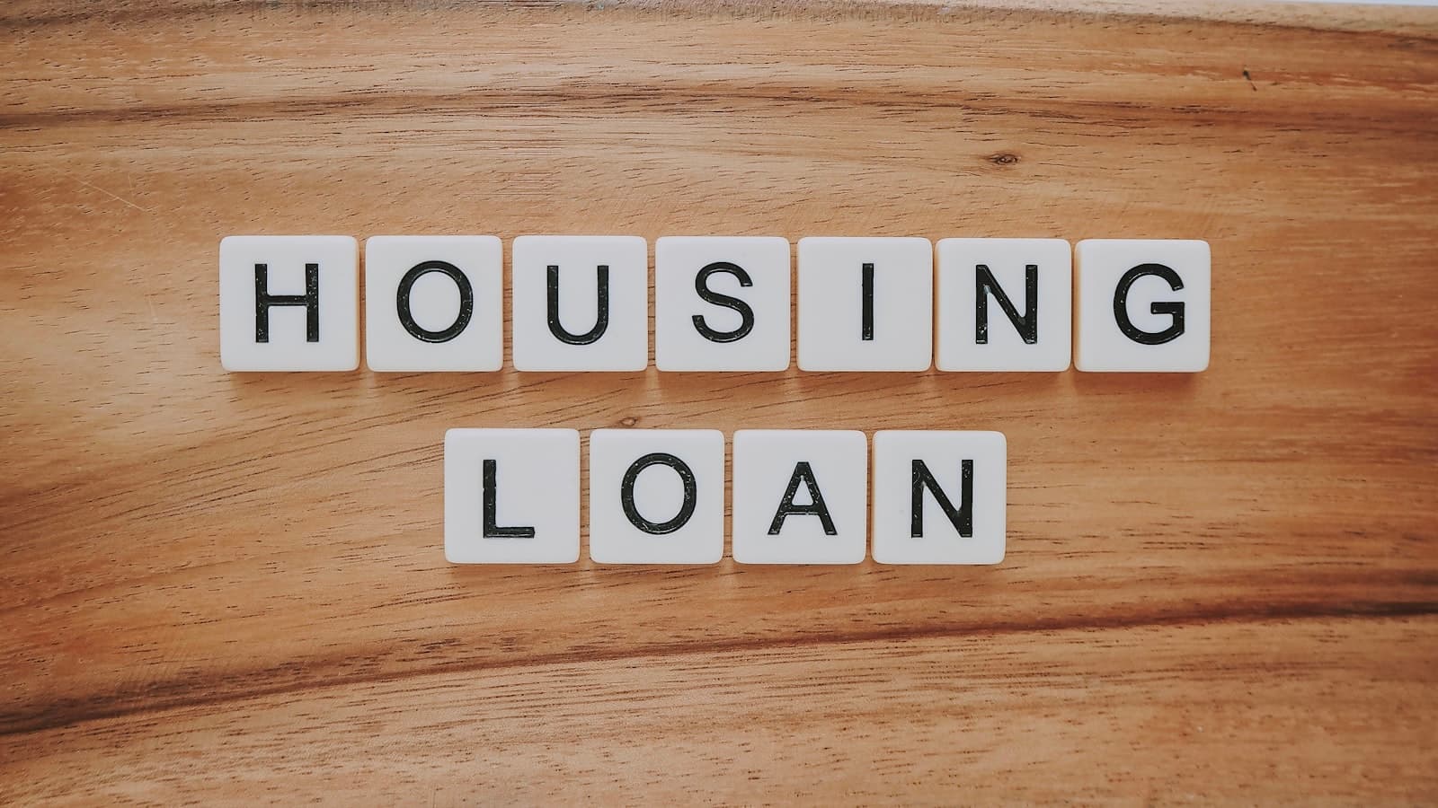 Wooden letter tiles spelling out HOUSING LOAN on a wood-grain surface