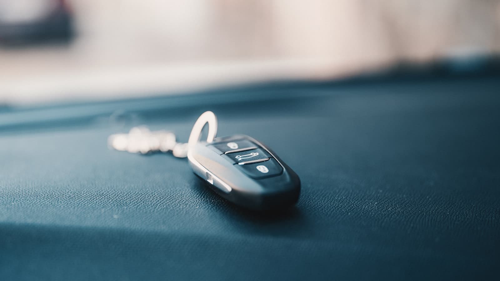 A close-up of a car key fob resting on a dark leather surface